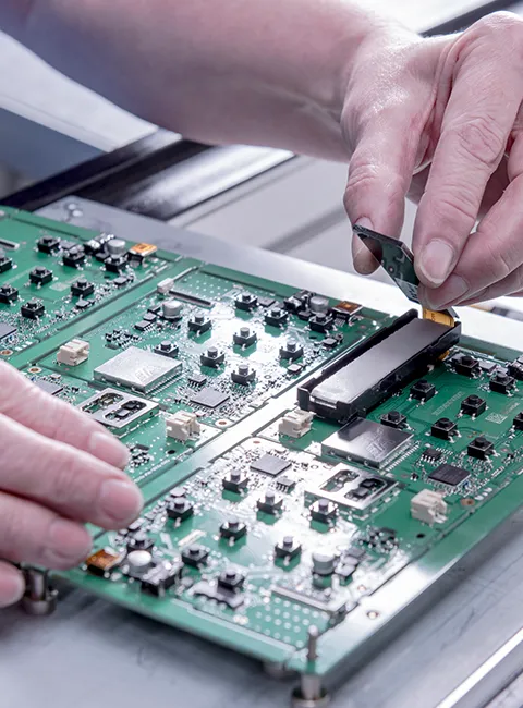 Ręce pracujące nad zieloną płytką drukowaną z elementami elektronicznymi w środowisku produkcyjnym.