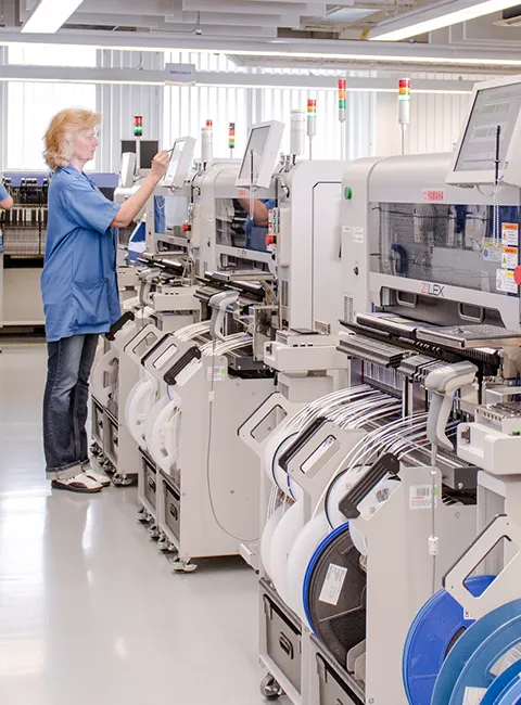 Pracownica obsługuje nowoczesne maszyny montażowe w jasnej hali produkcji elektroniki.