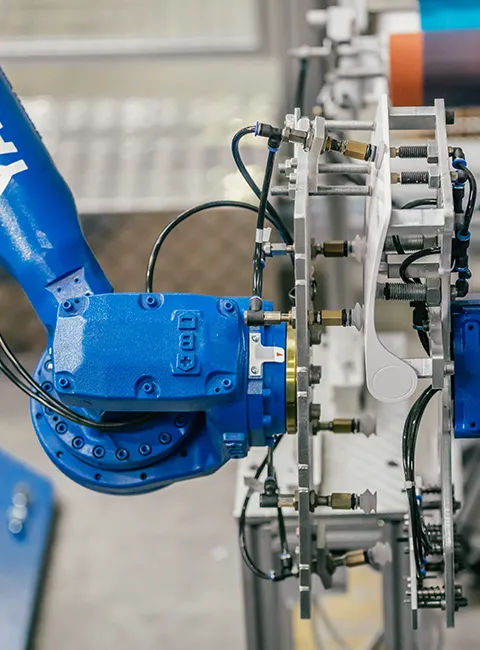 Niebieski ramię robota przemysłowego pracuje przy obracającym się urządzeniu w zautomatyzowanym środowisku produkcyjnym.