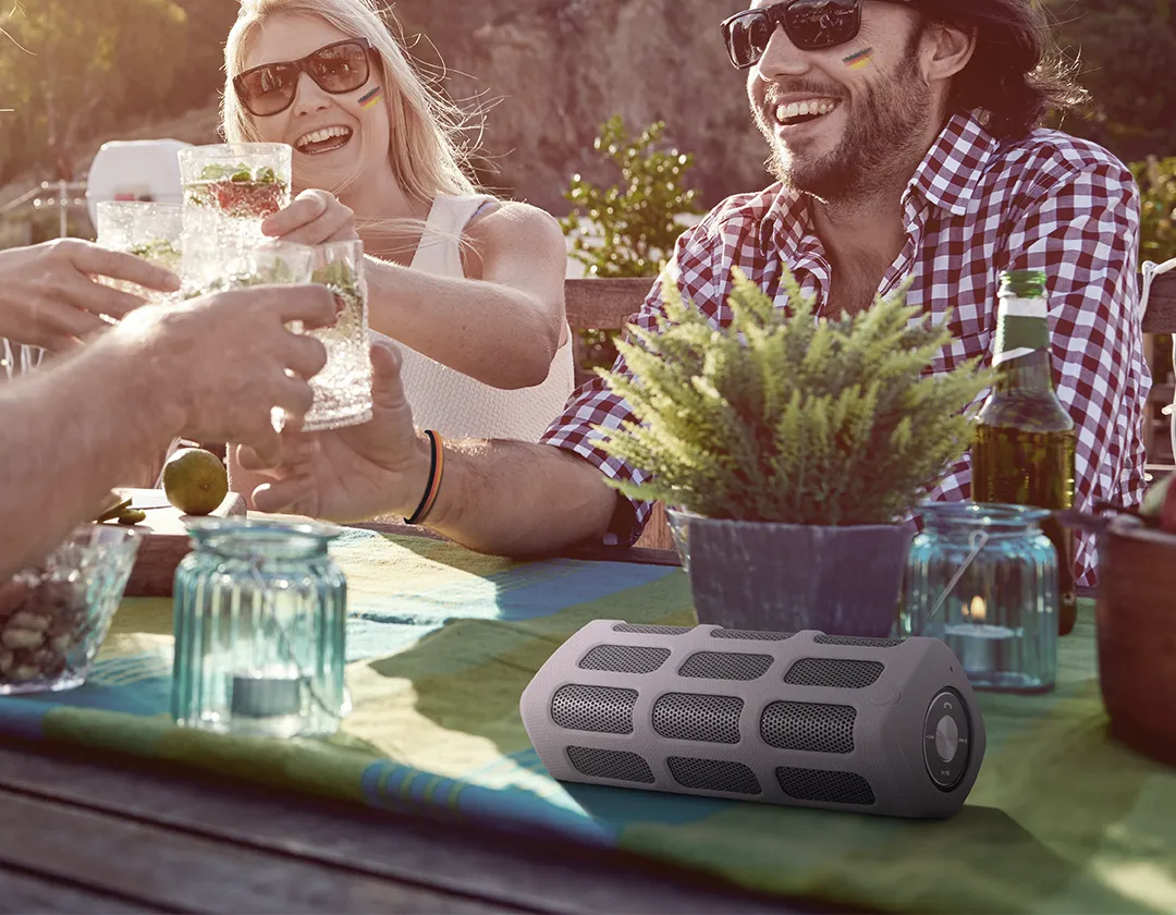 Eine Gruppe sitzt gut gelaunt an einem Tisch und hört Musik aus einem Bluetooth Lautsprecher der über einen Akku läuft.