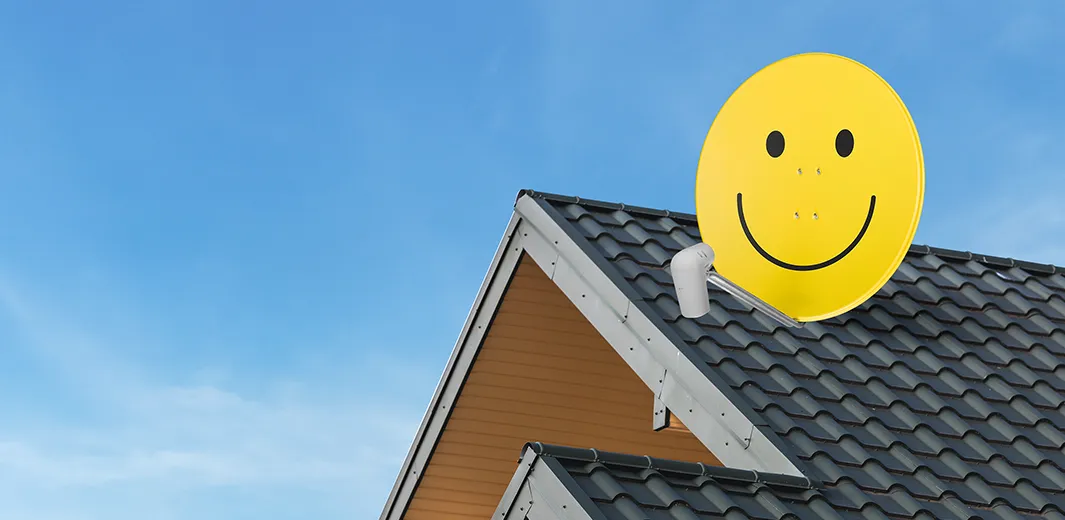 Eine TechniSat Satellitenschüssel mit ikonischem Smiley-Gesicht in gelber Farbe auf einem Dach ermöglicht TV-Empfang.