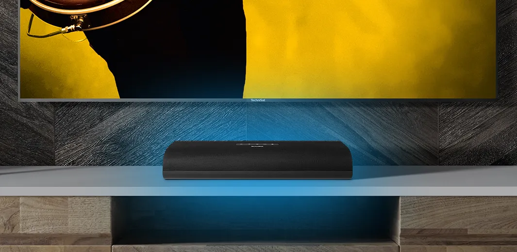 Soundbar von TechniSat steht im Wohnzimmer auf einem Regal vor TV-Gerät und sorgt für exzellenten Klang.