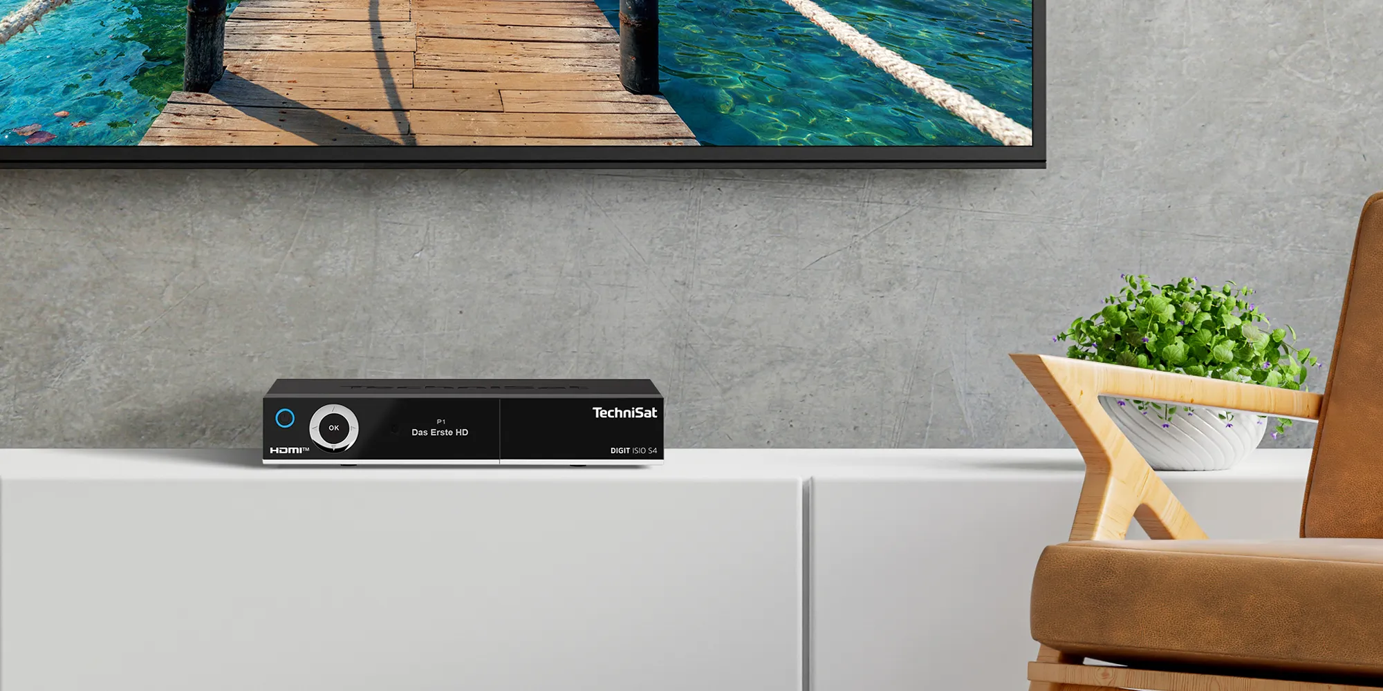 TechniSat Receiver steht auf Regal in einem Wohnzimmer vor einem TV mit maritimen Bildinhalt.