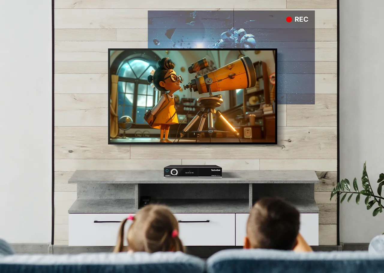 Kinder gucken im Wohnzimmer vor einem TV mit Receiver ihr Programm, während der Receiver ein anderes parallel aufnimmt.