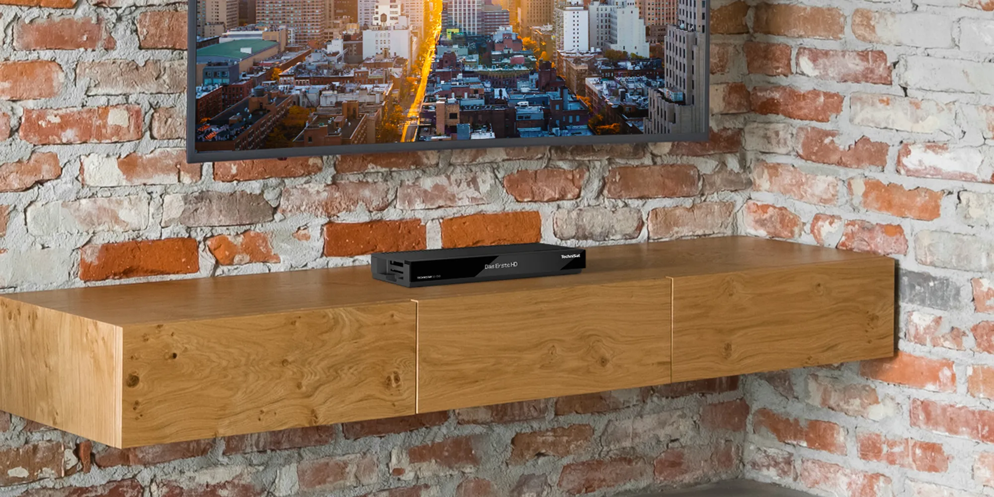 TechniSat Receiver für Satellitenempfang steht auf einem Holzregal vor einem TV, dessen Bild eine Großstadt zeigt.