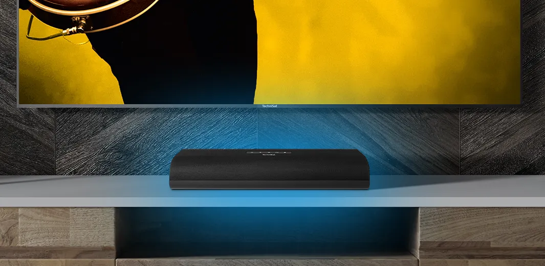 Soundbar von TechniSat steht im Wohnzimmer auf einem Regal vor TV-Gerät und sorgt für exzellenten Klang.