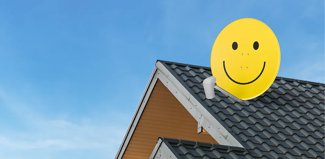 Eine TechniSat Satellitenschüssel mit ikonischem Smiley-Gesicht in gelber Farbe auf einem Dach ermöglicht TV-Empfang.